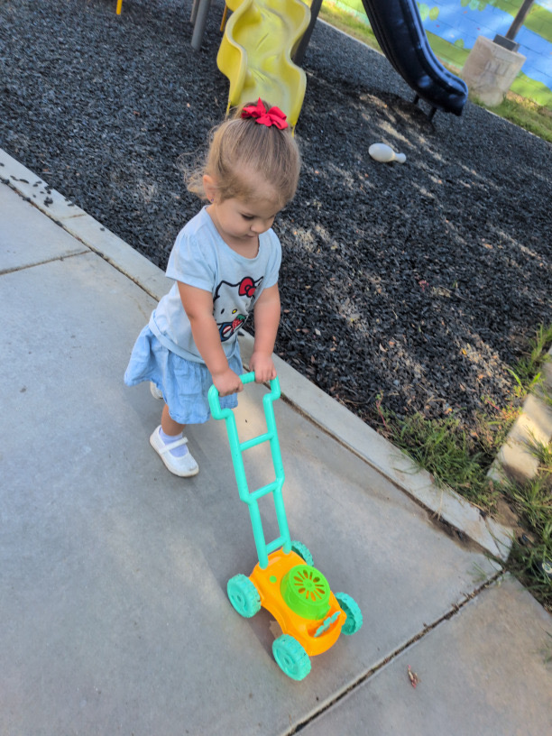 A child pushing a toy lawn mower on the playground path