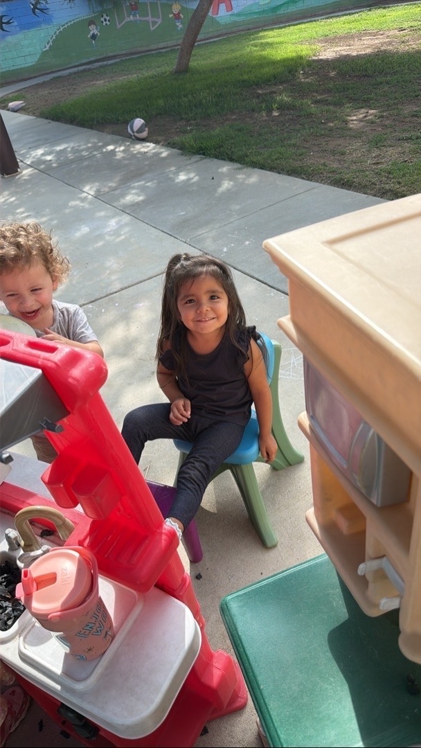 Children smiling beside the outdoor play kitchen