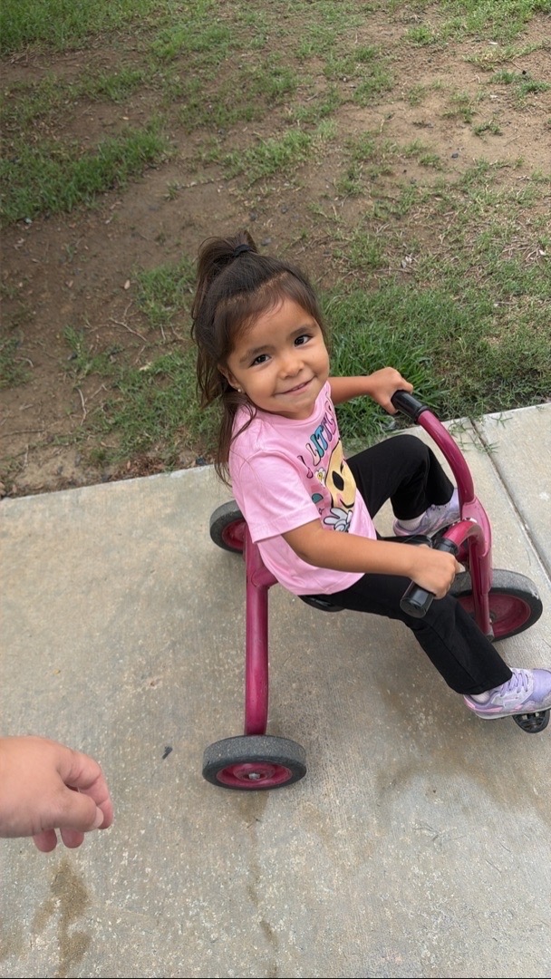 A smiling child sitting on a playground tricycle