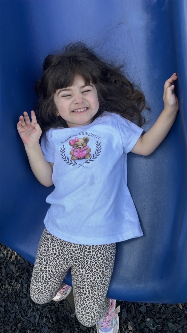 A child grinning on the blue playground slide