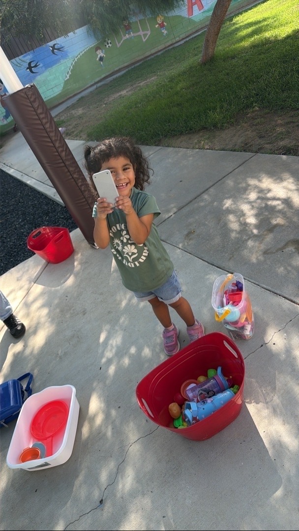 A child playing with cups and pretend food at an outdoor table