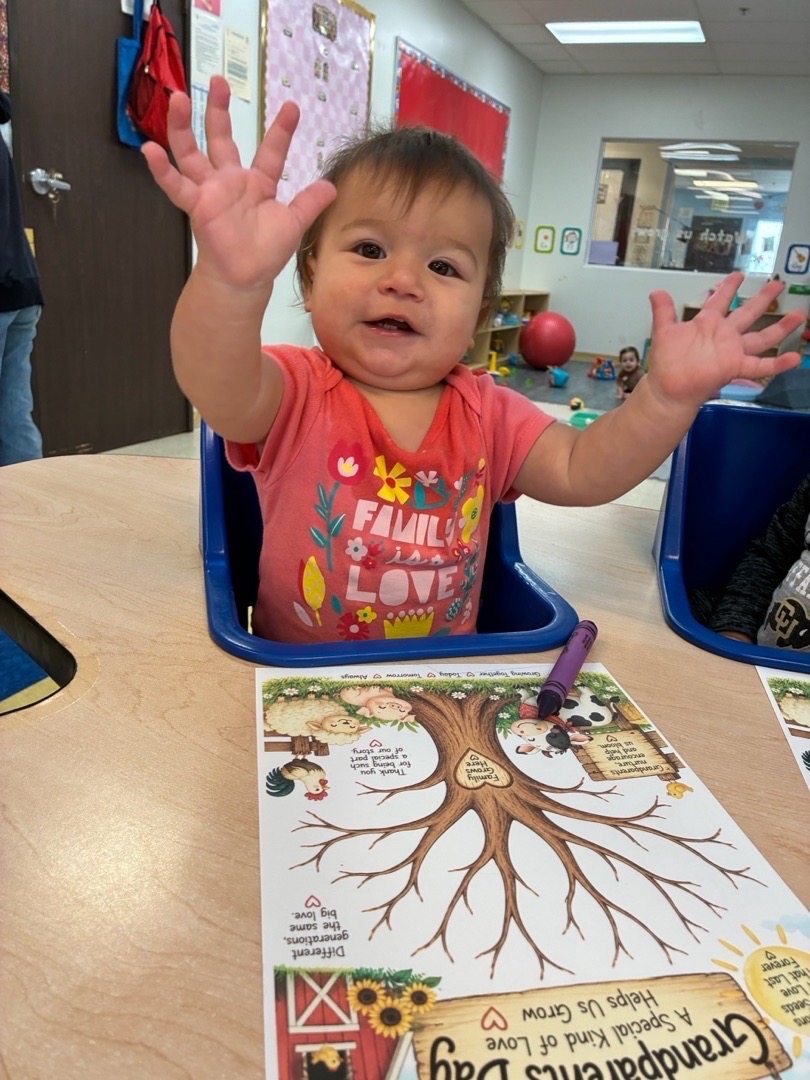 A child raising both hands at an art table