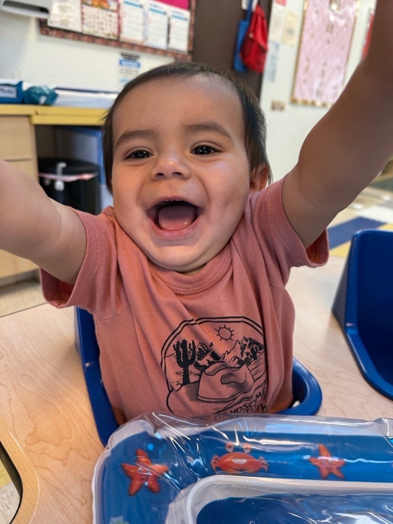 A smiling child raising both arms over a sensory water mat