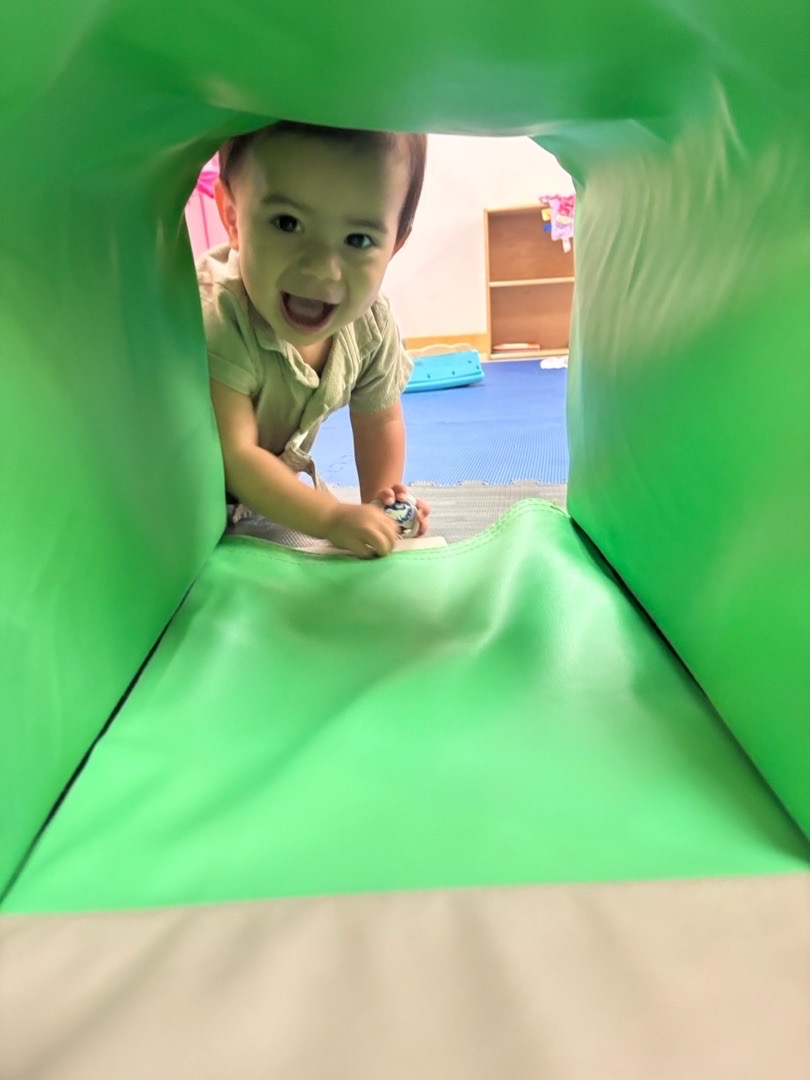 A child smiling from a green play tunnel