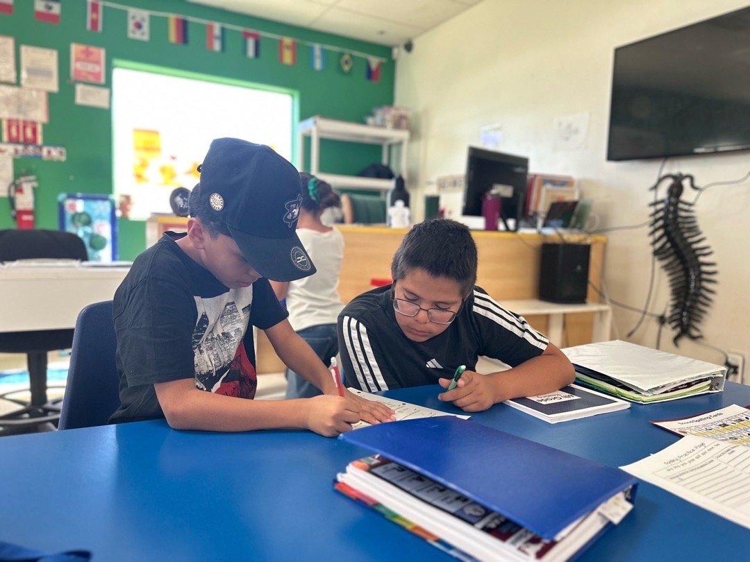 Two children working together on a paper at a classroom table