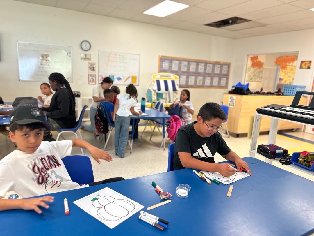 Children decorating pumpkin pictures at a classroom table