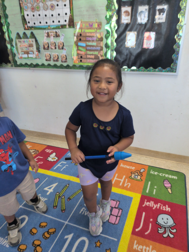 A smiling child holding a blue classroom pointer
