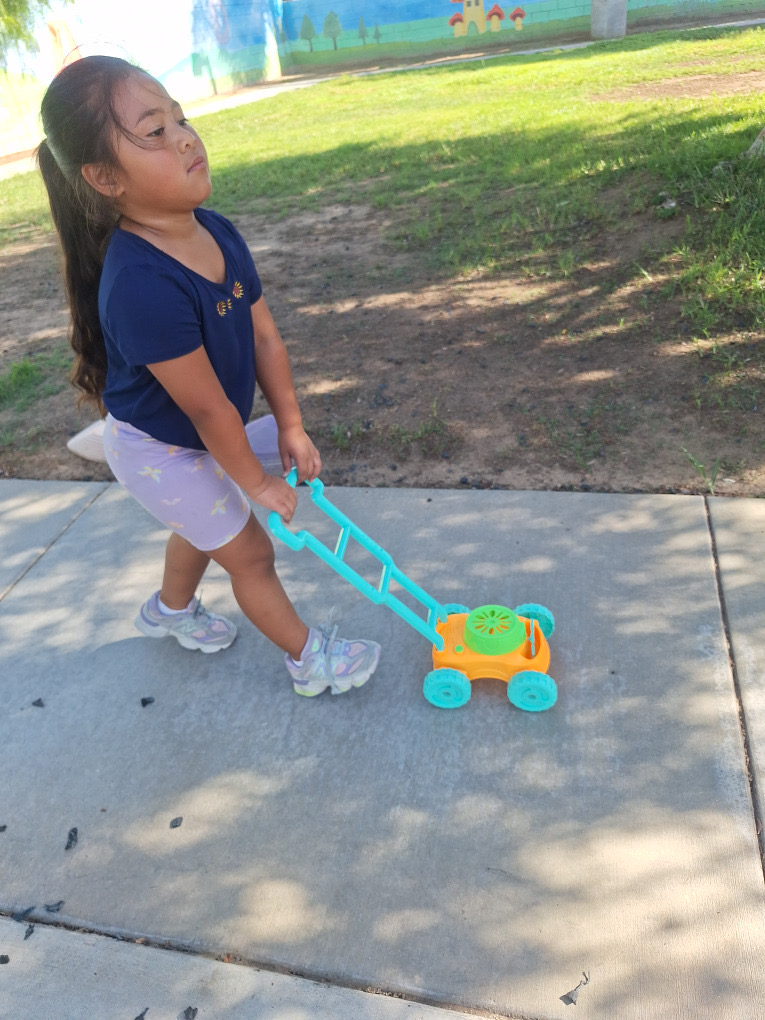 A child pushing a colorful toy lawn mower outside